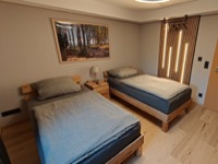Schlafzimmer 1 mit zwei Einzelbetten aus Eiche und beleuchteter Holz-Lamellenwand