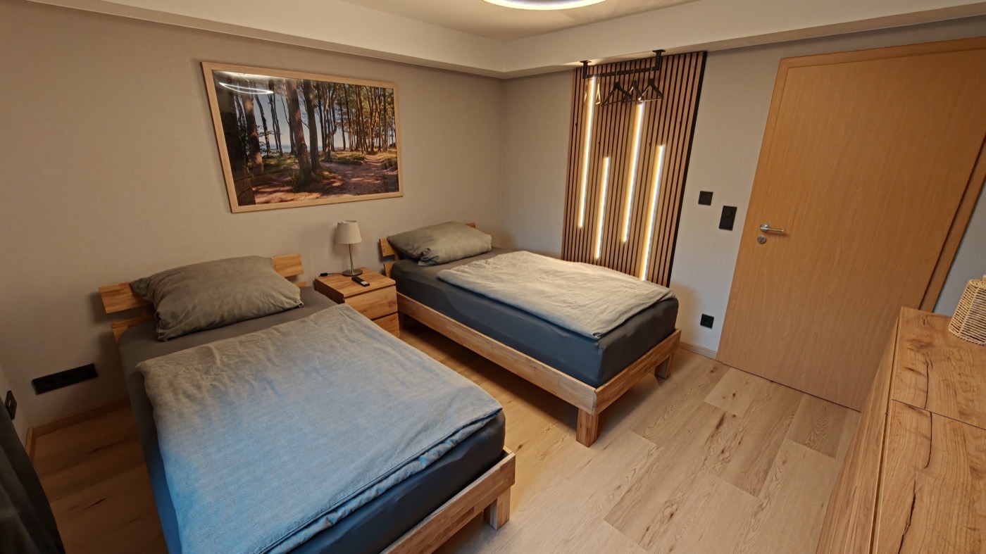 Frisch renoviertes Schlafzimmer mit Massivholzbetten und beleuchteter Holz-Lamellenwand